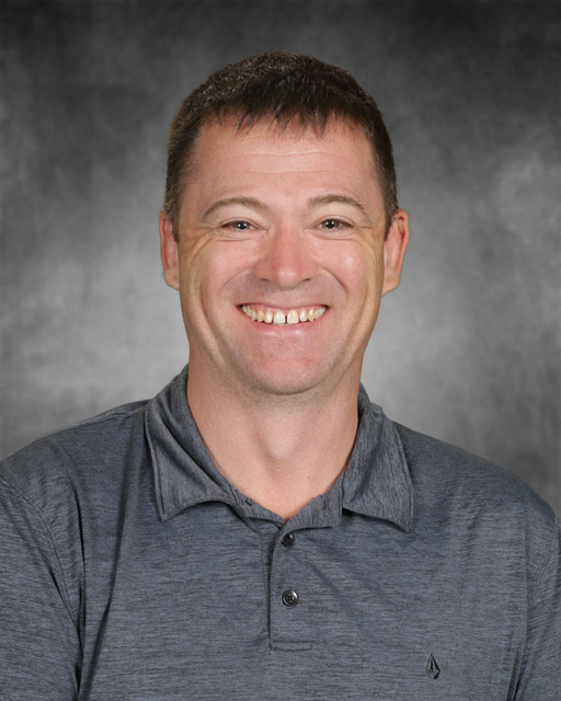 Portrait of a smiling man with short brown hair wearing a gray polo shirt.