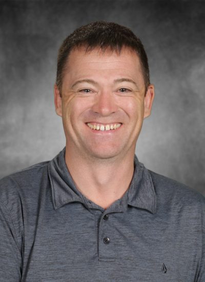 Portrait of a smiling man with short brown hair wearing a gray polo shirt.